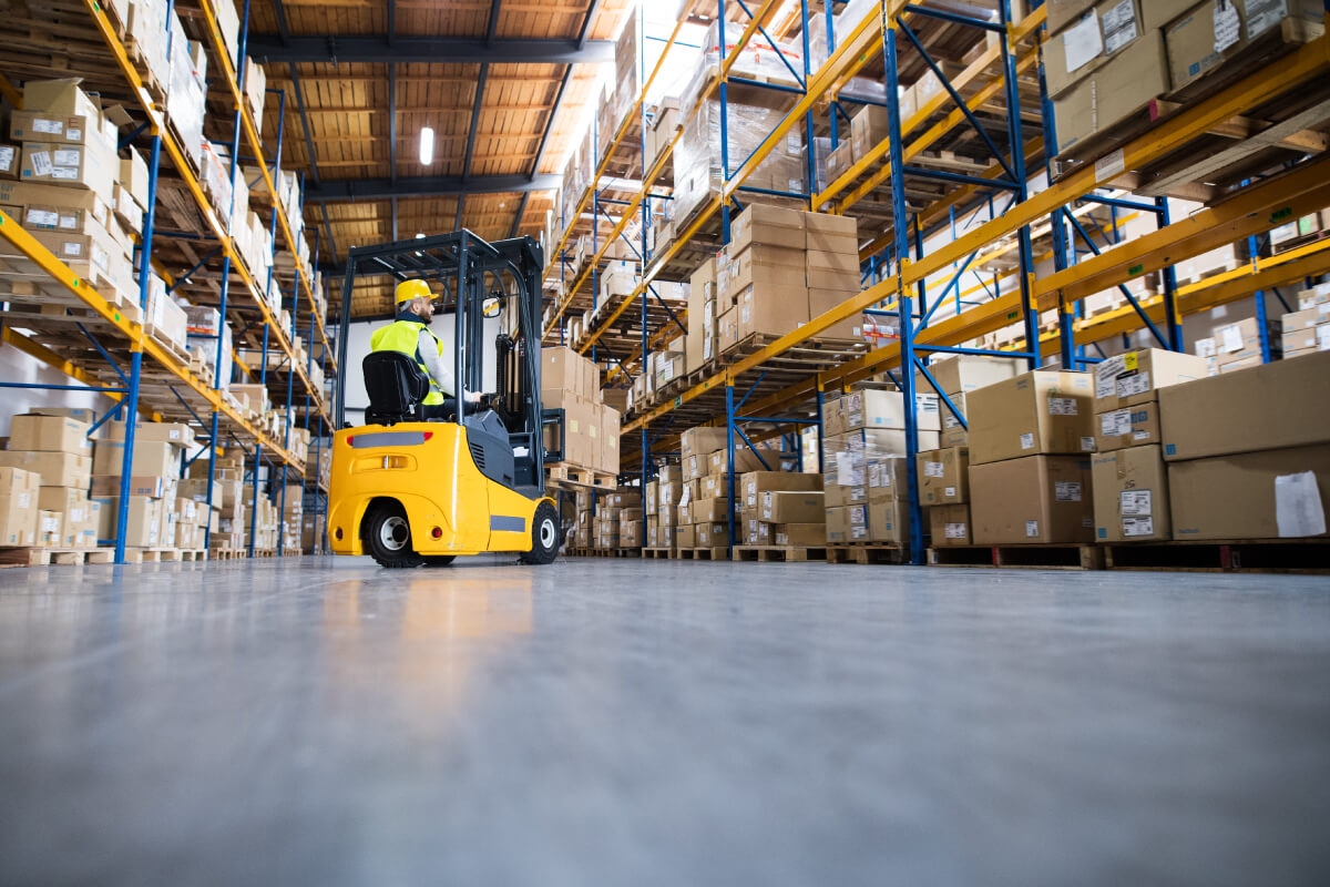 Warehouse male worker on forklift between rows of tall shelves full of packed boxes and goods