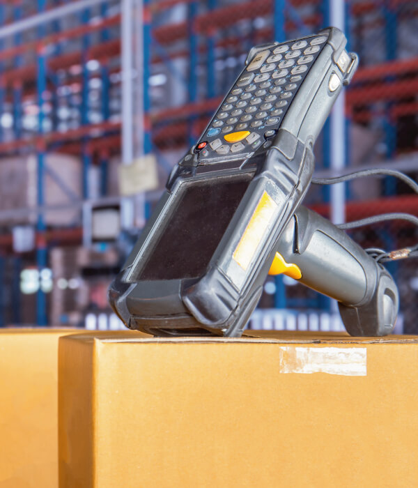 RF Scanner sat on top of cardboard box, blurred warehouse shelving in the background