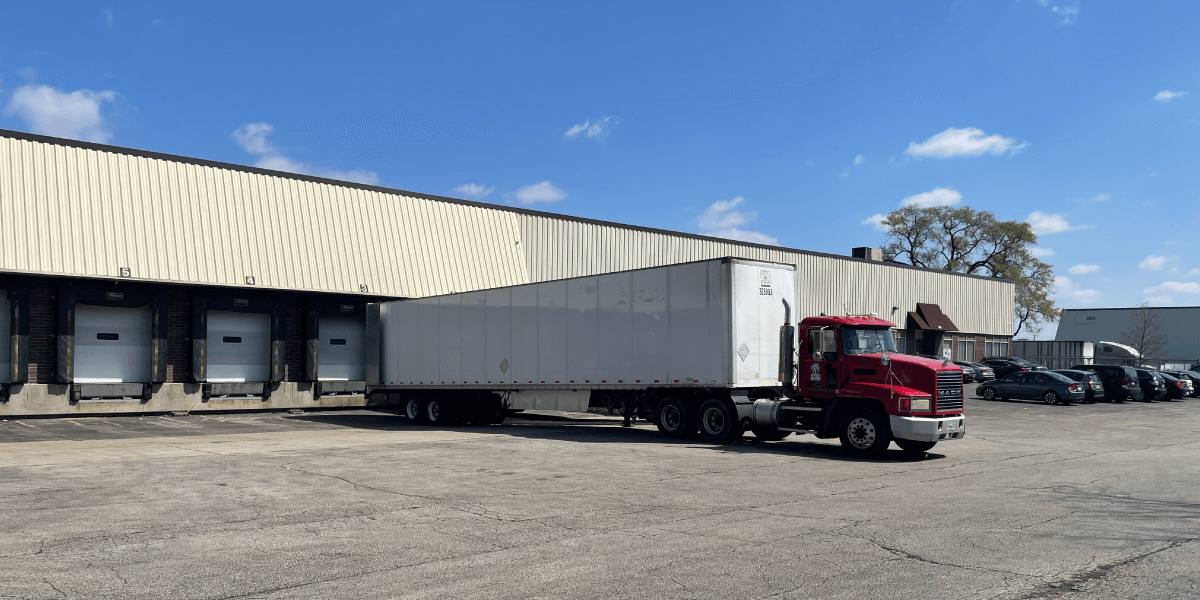 A red and a white truck at a freight loading dock with blue sky and clouds overhead